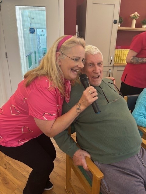 A woman and older gentleman singing into a microphone