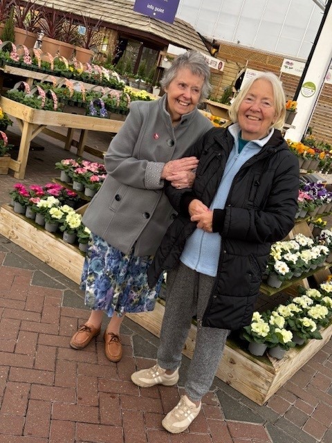 Two woman in coats stood in front of a display of flowers