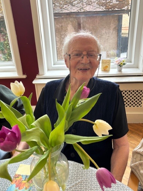 An older gentleman smiling with a vase of tulips
