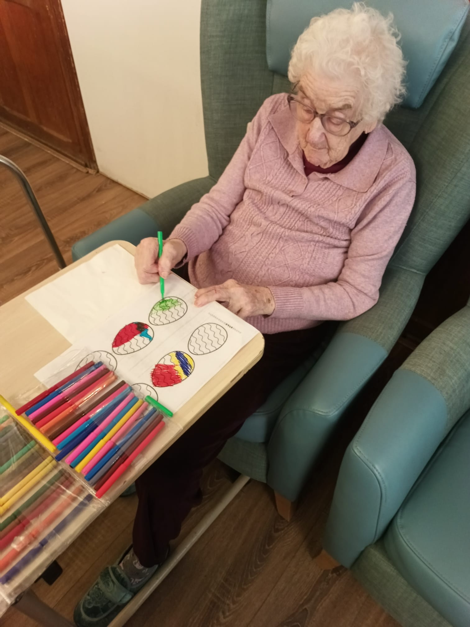 An older woman sat in an armchair colouring in a picture