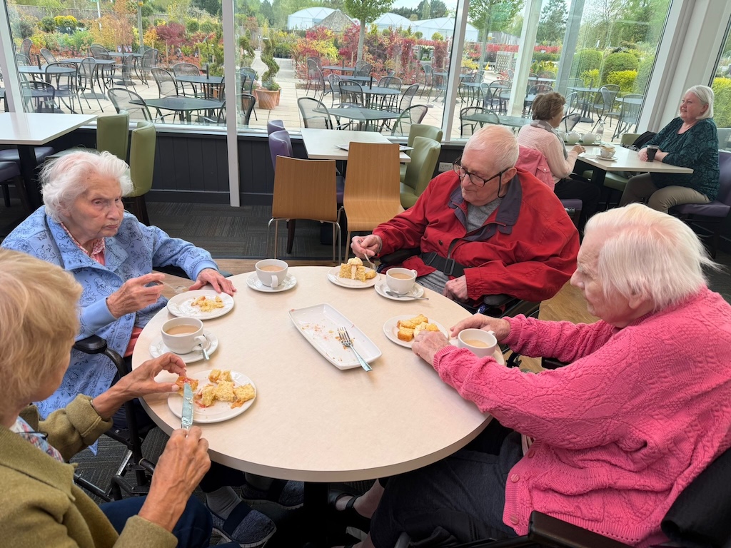 A group of people sat around a table in a cafe having tea and cake