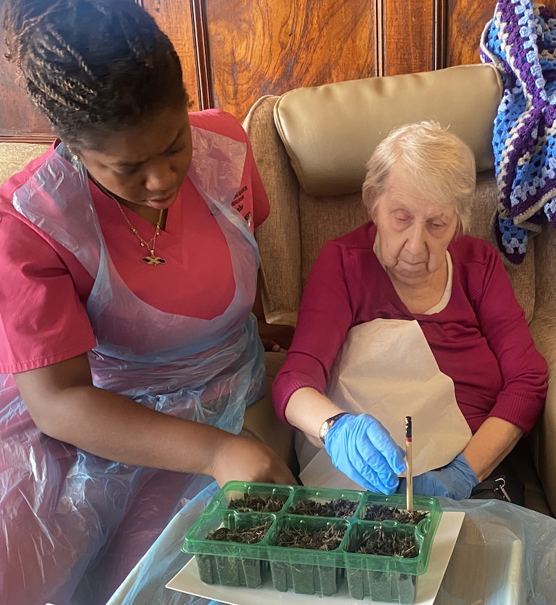 A older woman and staff member planting seeds in a tray of soil