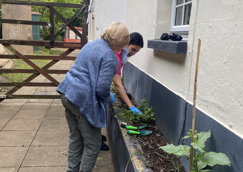 An older woman and staff members digging plants in a flower bed