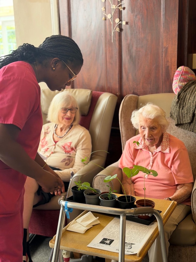An older woman looking at plants in pots on a table while a staff member stands talking to her