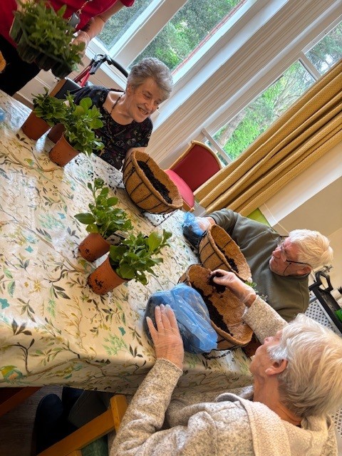 A group of people sat around a table planting hanging baskets