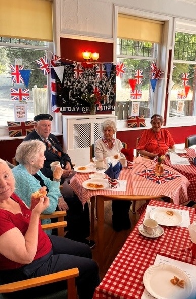 A group of people sat around a table having refreshments with bunting strung around the room