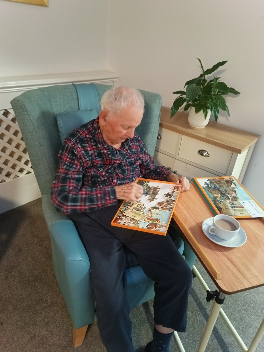 An older man sat in a chair doing a puzzle