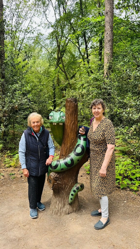 Two woman in a forest stood by a snake sculpture