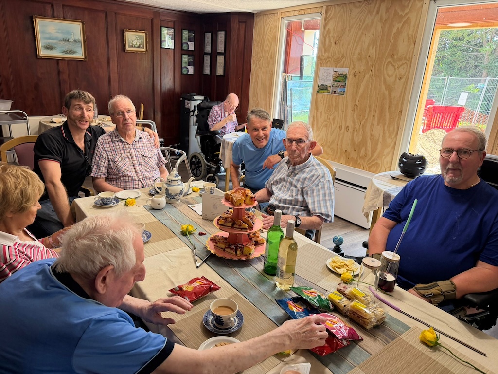 A group of people sat around a table having afternoon tea.