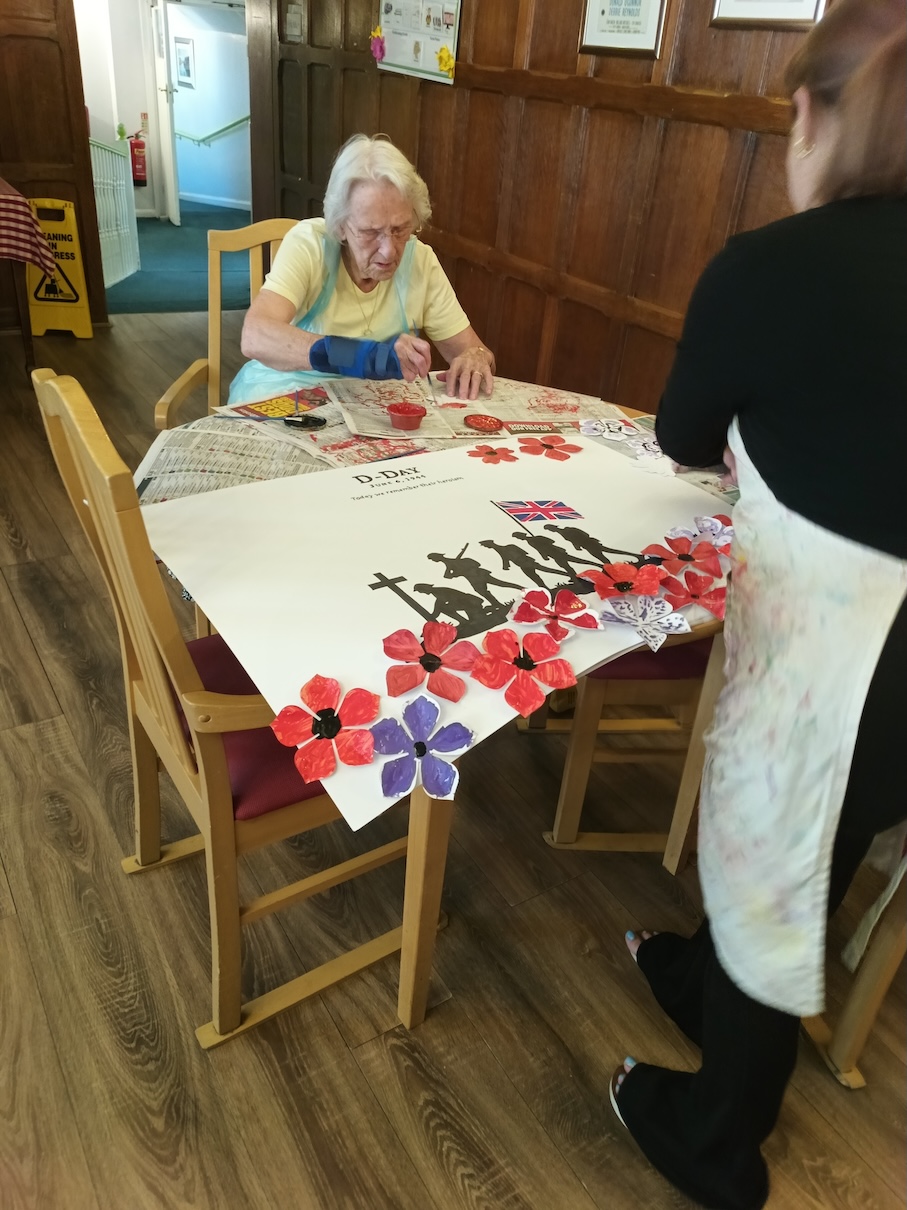 An older woman sat at a table painting a picture with poppies