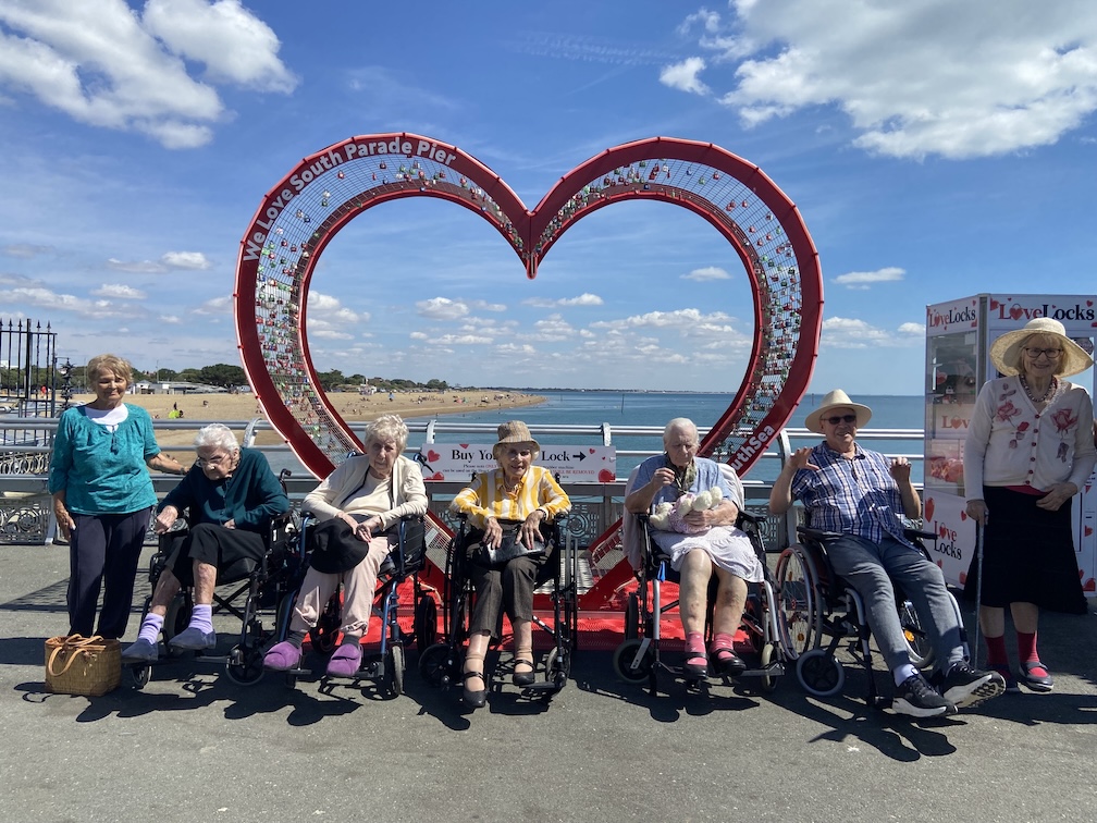 A group of older people in wheelchairs stood in front of a giant heart 