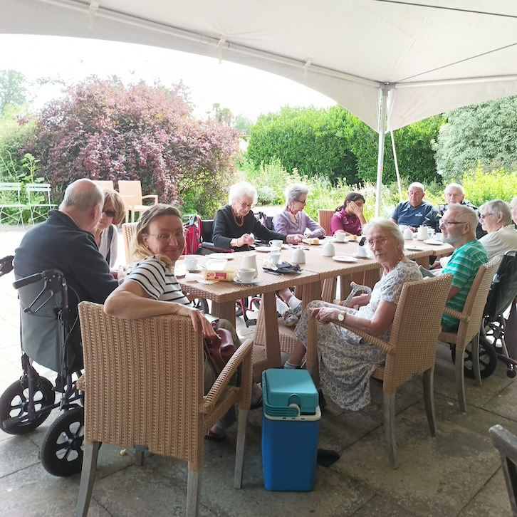 A group of people sat around a large outdoor table with refreshments