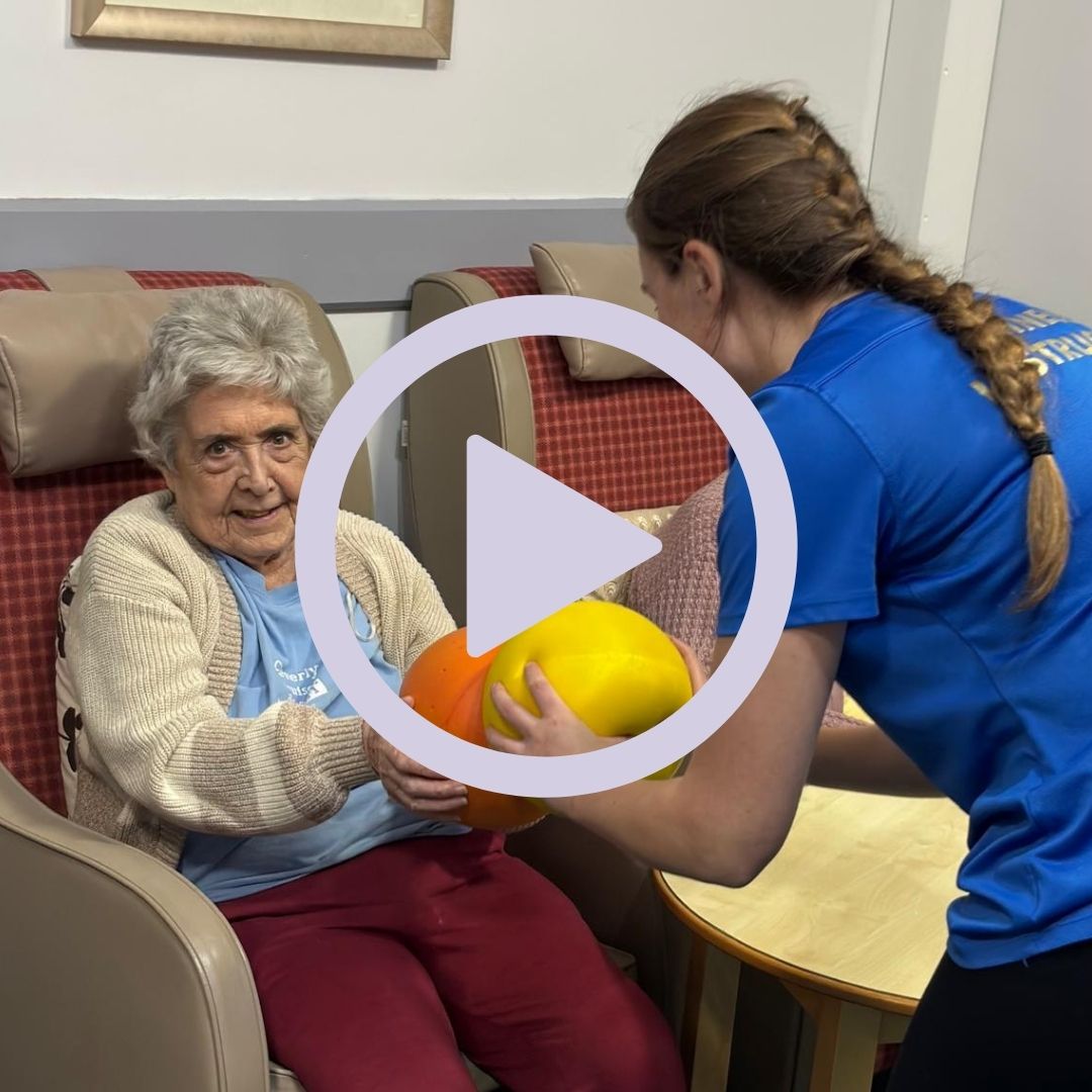 An older man being shown an exercise using a ball 