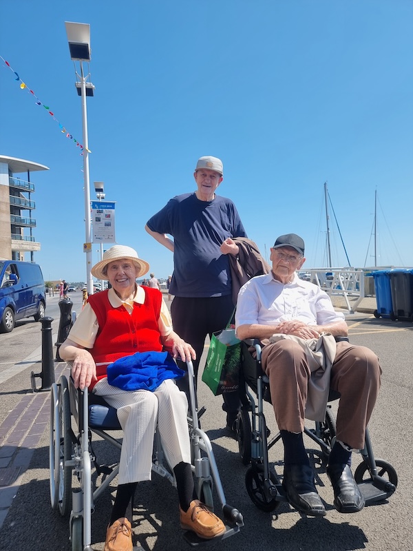 A group of people at the quay in the sunshine with boats in the background