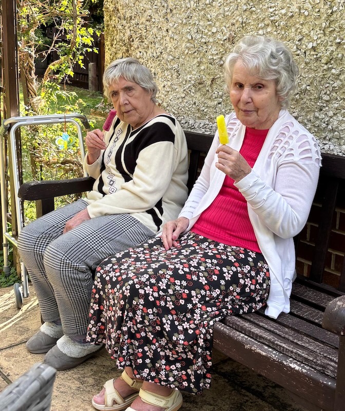Two ladies sat on a garden bench eating an ice lolly