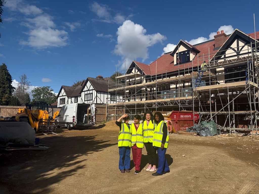 A group of people in hi-vis vests stood in front of a building covered in scaffolding 
