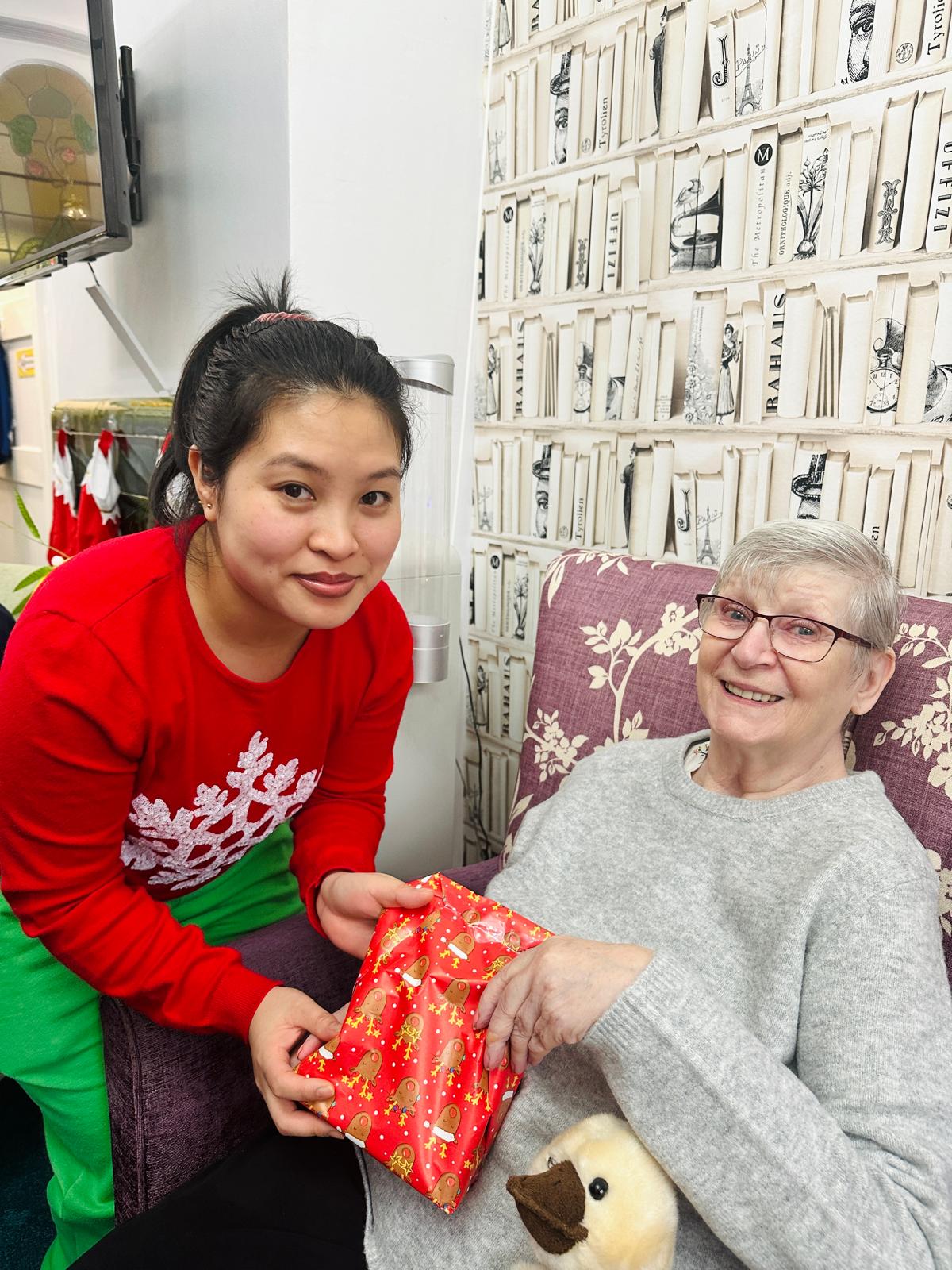 A woman wearing red giving a gift to an elderly woman. 
