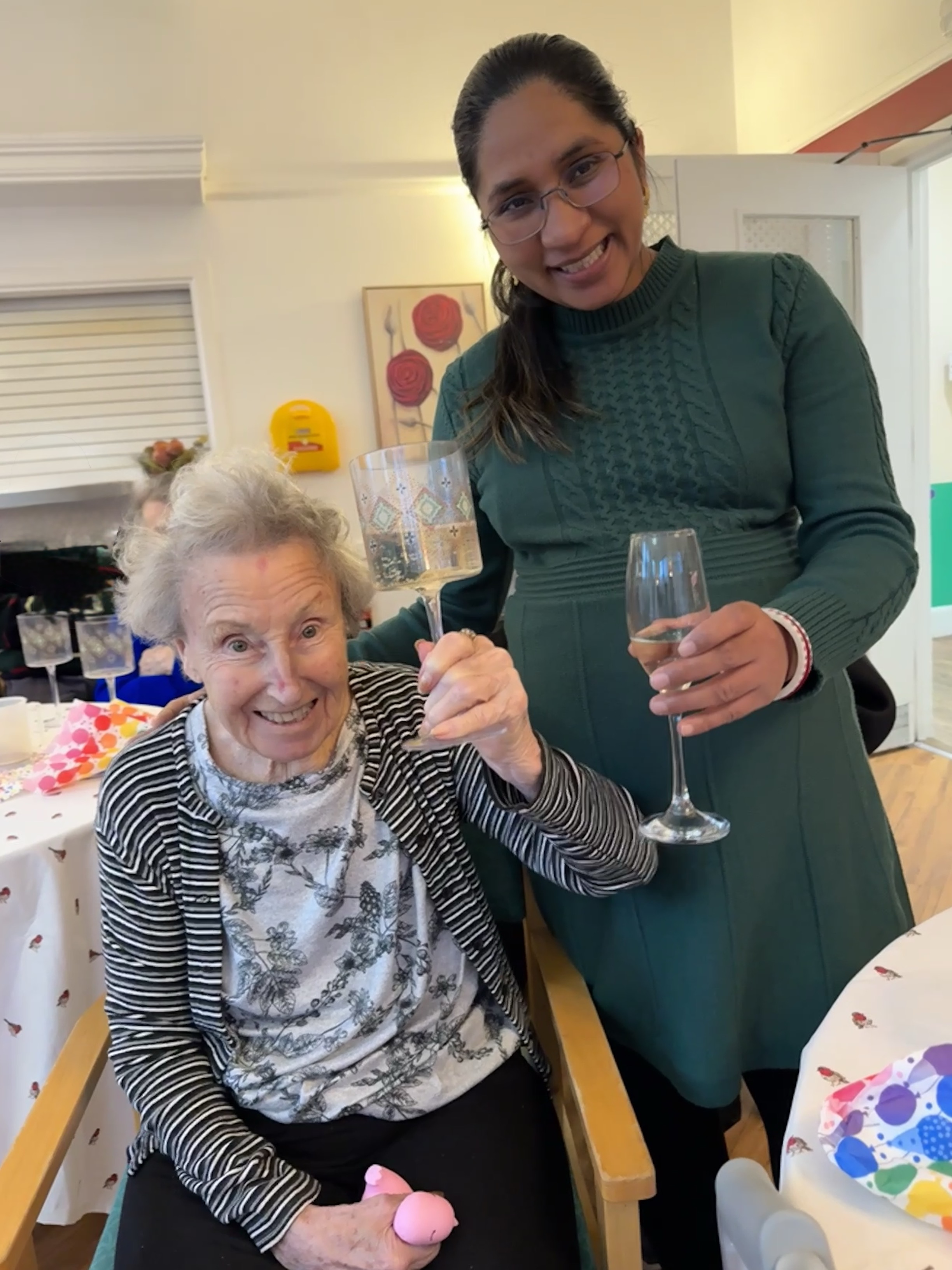 A pregnant woman wearing green stood next to a very happy elderly woman.