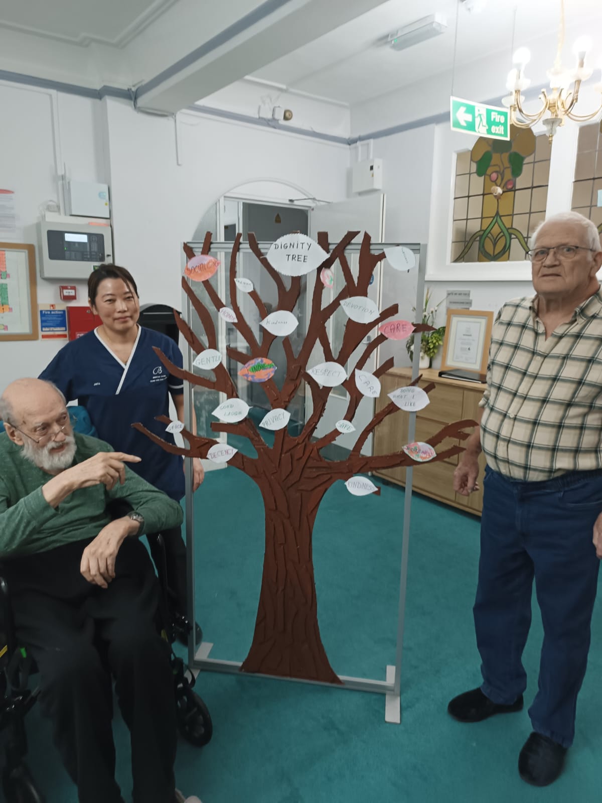 People stood around an artificial tree with pieces of paper attached to the branches.