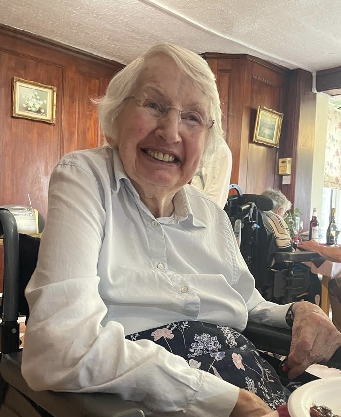 A happy woman smiling sat in a chair wearing a light coloured blouse