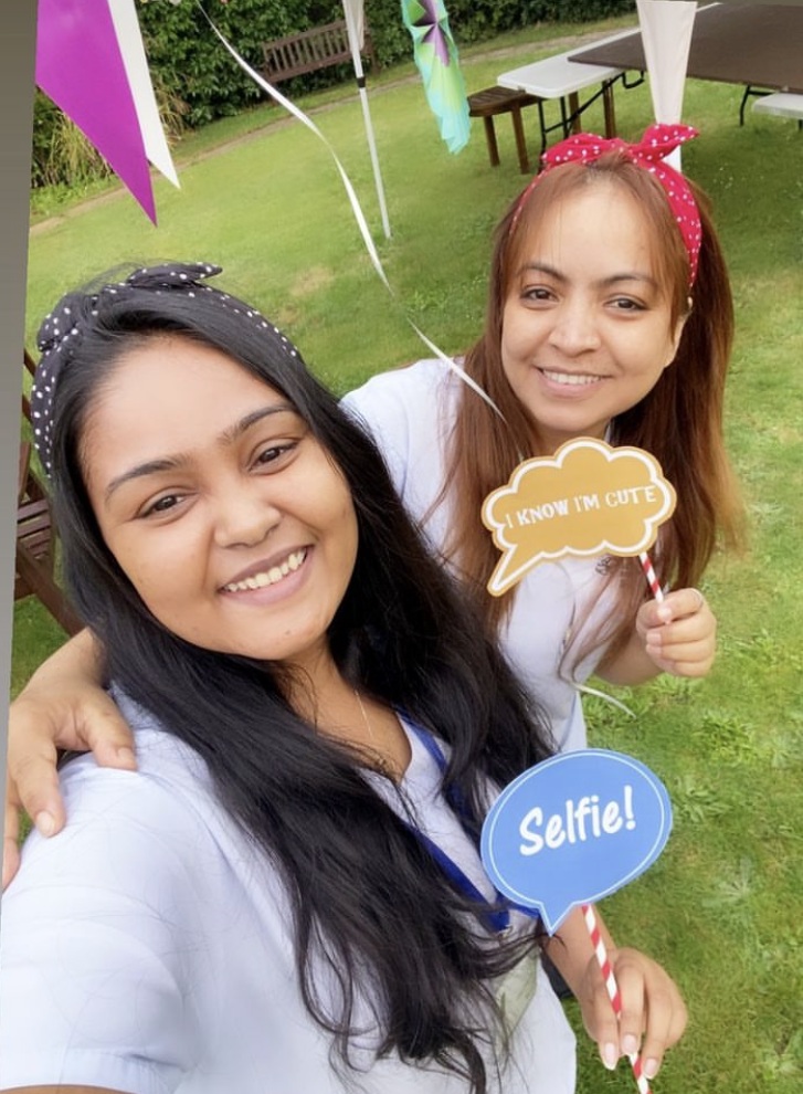 Two smiling young women holding small signs saying "Selfie!" and "I know I'm cute"