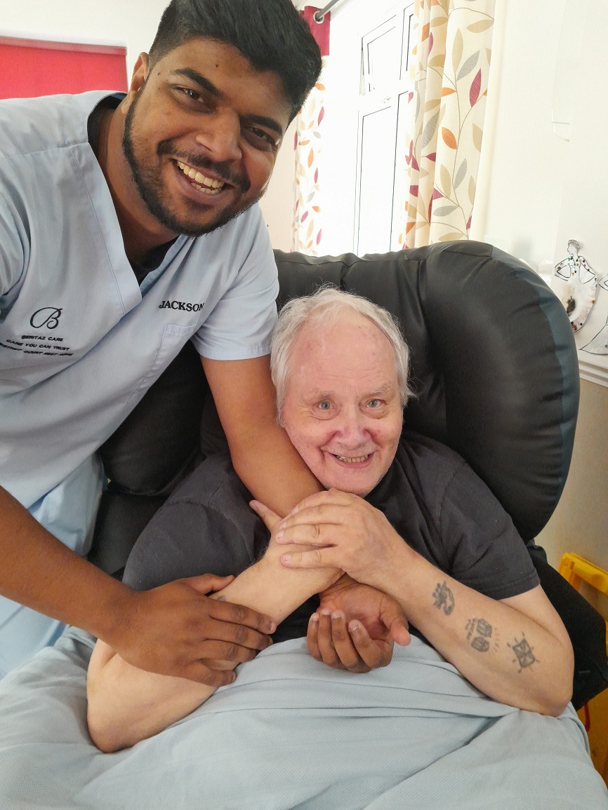 A man wearing a blue care uniform and a person in a comfortable chair.