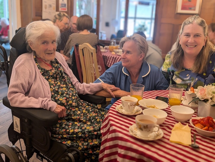 Elderly woman sat with staff having a cup of tea and refreshements at a party