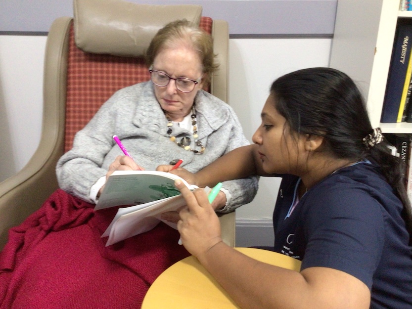 Resident writing in a book with the help of a staff member