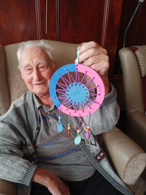 Elderly man holding up a hand crafted dreamcatcher