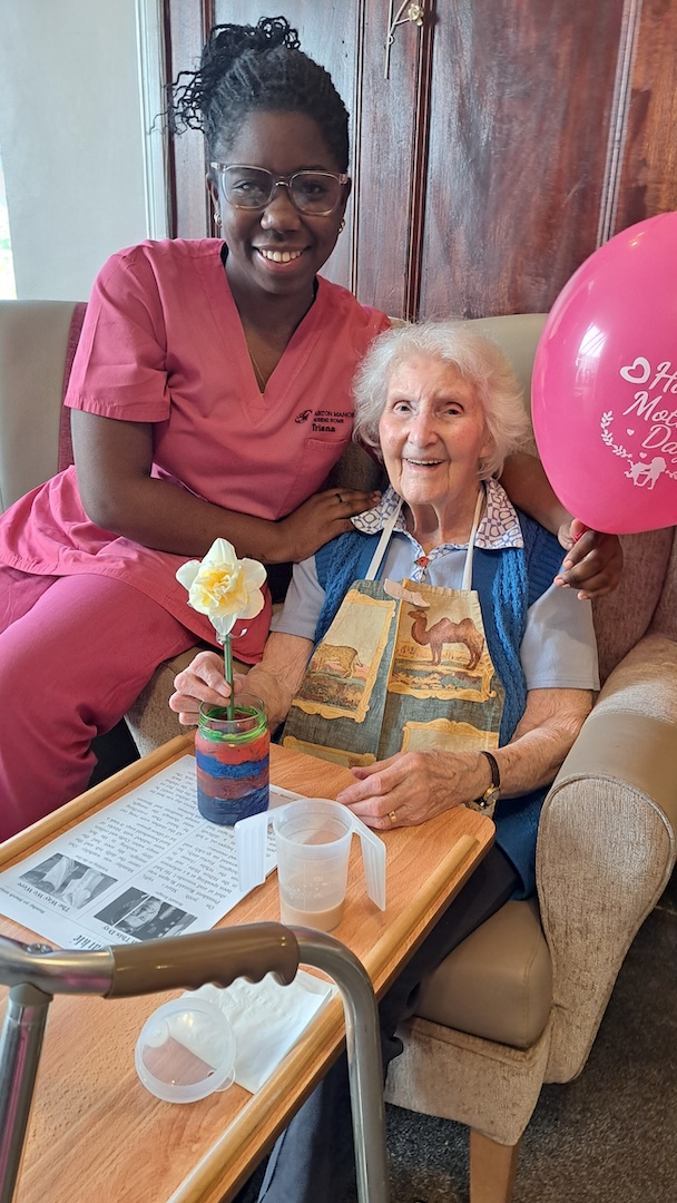 Elderly woman sat with staff member holding a balloon and smiling