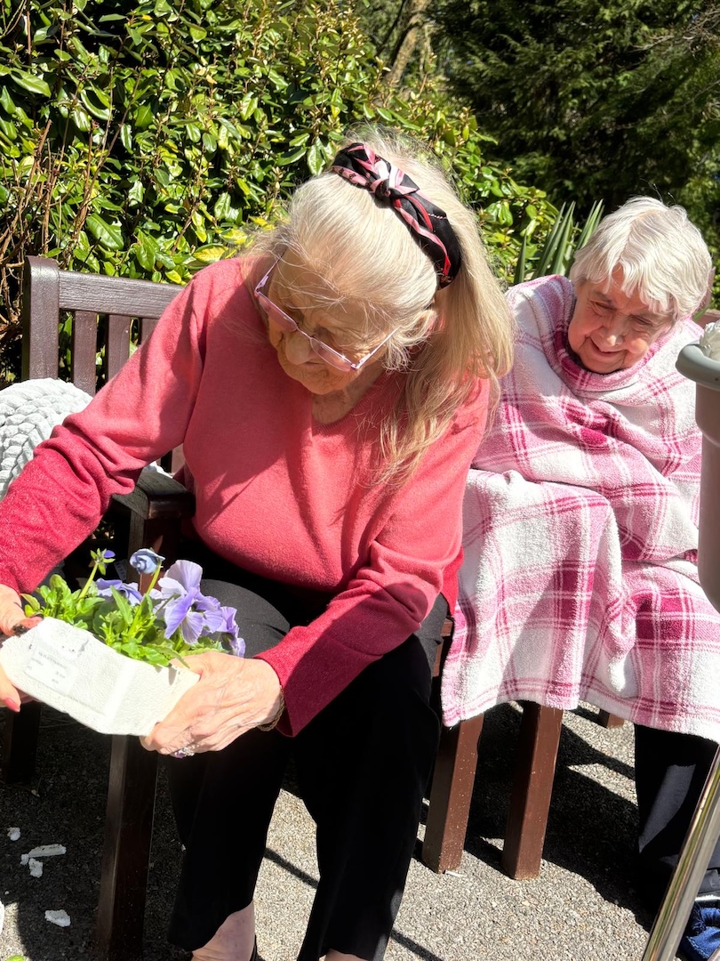 Two elderly women sat on a garden bench planting flowers