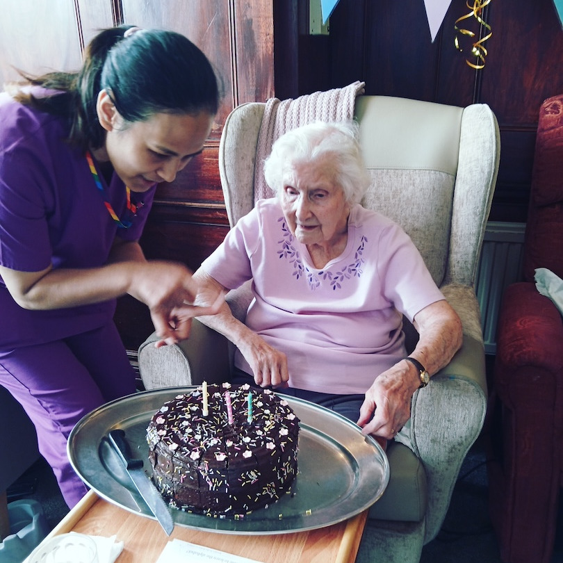 Elderly woman being presented with a birthday cake by a staff member