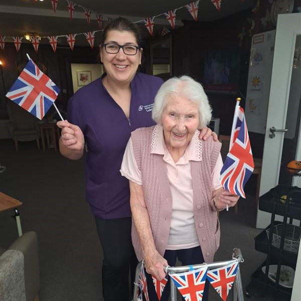 Resident and staff member smiling waving Union Jack flags