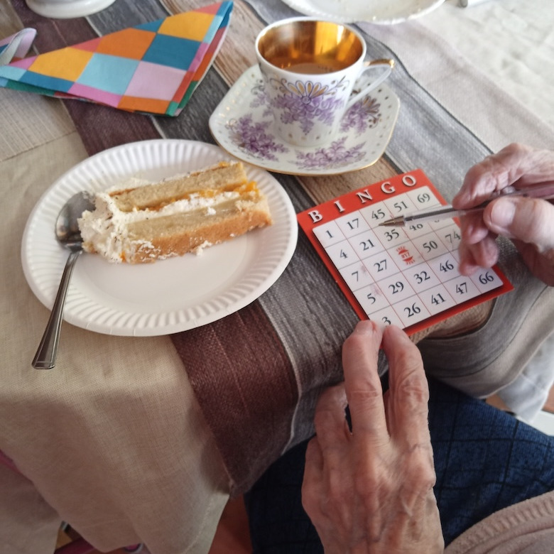 An older person playing bingo with a cup of tea and slice of cake