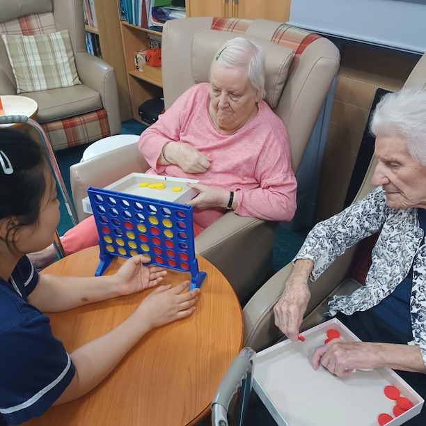 Staff member playing a board game with two older ladies sat in a lounge