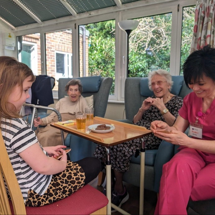 A group of older ladies, staff and a child sat at a table smiling and laughin