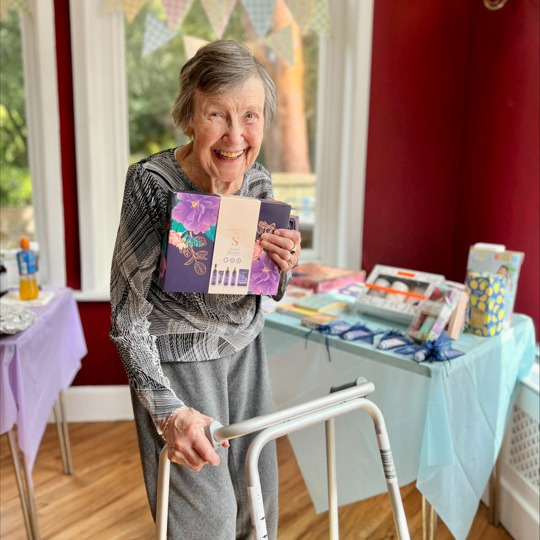 An elderly lady with a walking aid, smiling and holding a gift