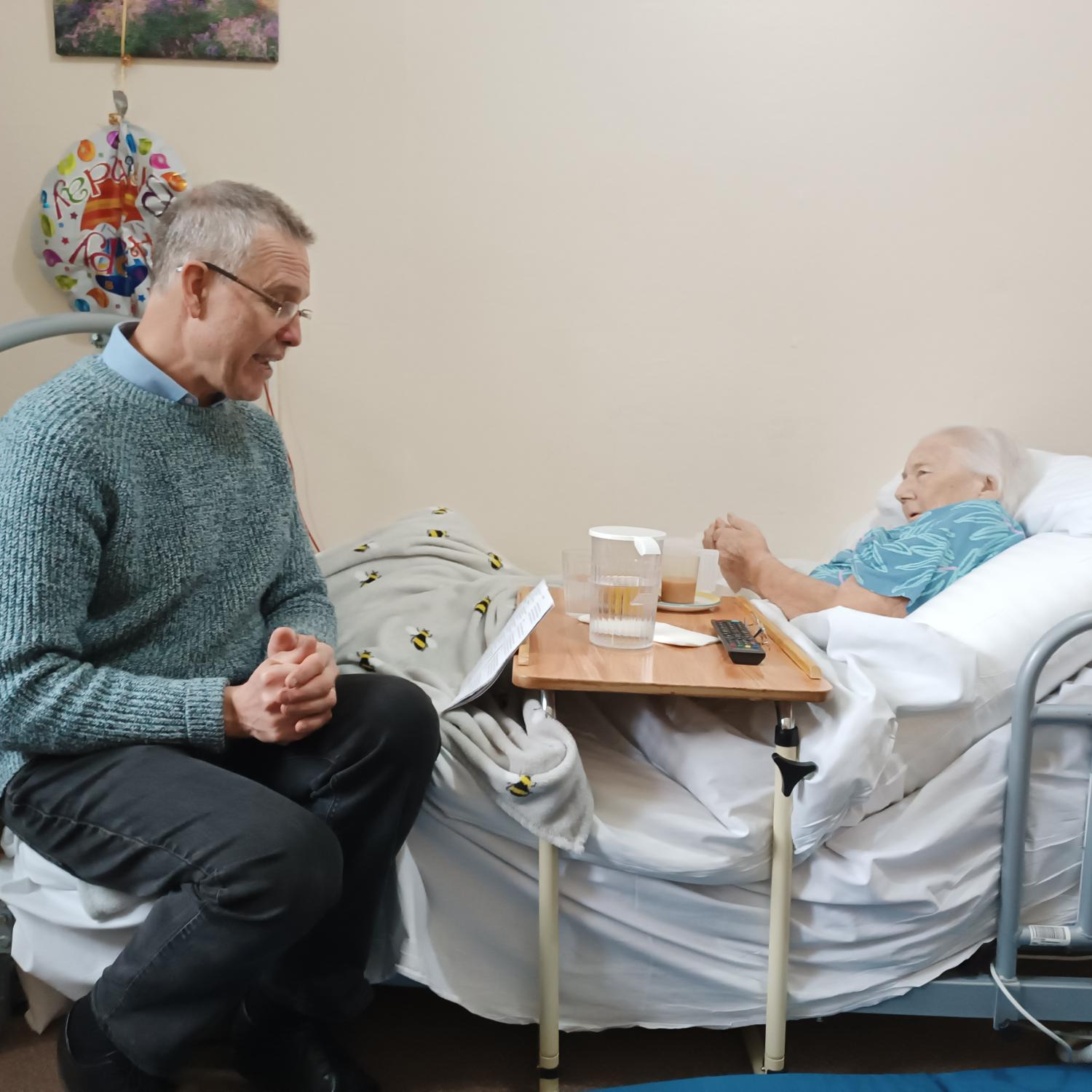 A man talking to an elderly lady laying in a bed