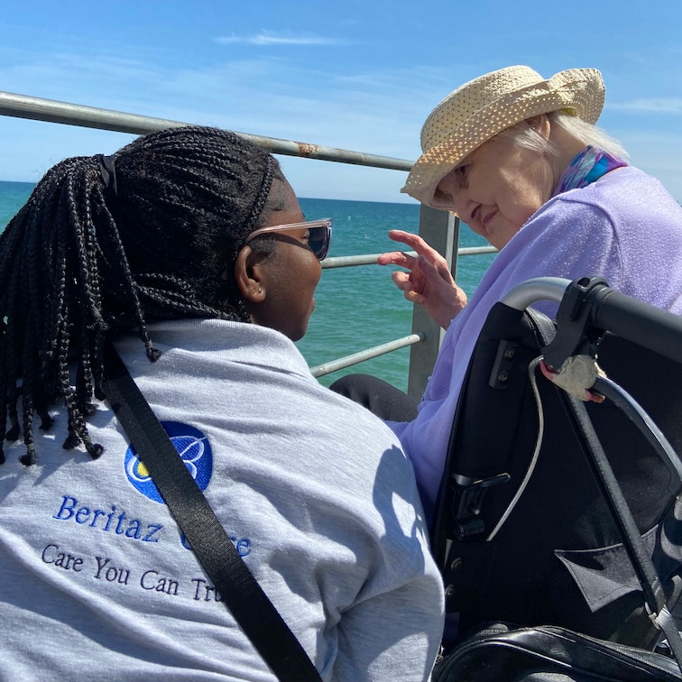 A staff member and lady in a wheelchair looking at the sea