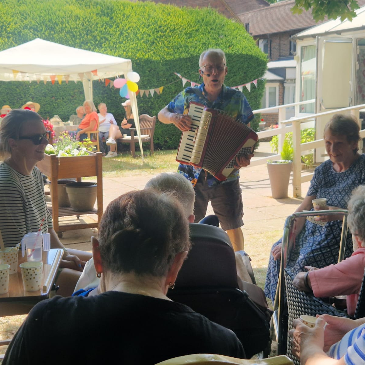 Party guests watching a musician playing an accordion in a garden