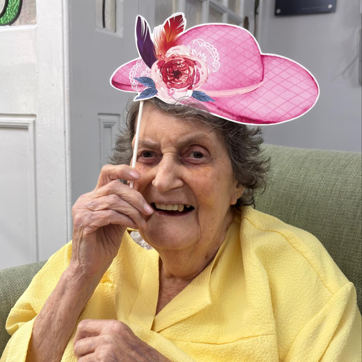 An older lady posing with a photo prop of a pink hat paper cut out