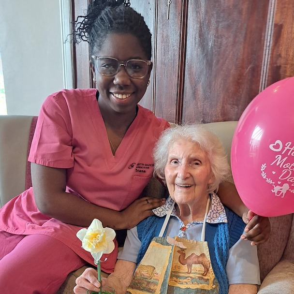 A staff member and elderly lady sat together smiling 