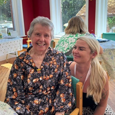 An older woman and staff member sat together smiling