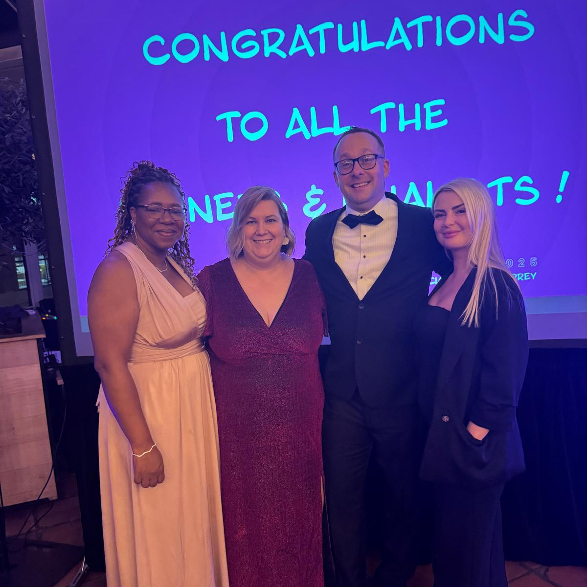 A group of people in formal wear in front of a screen at an awards event