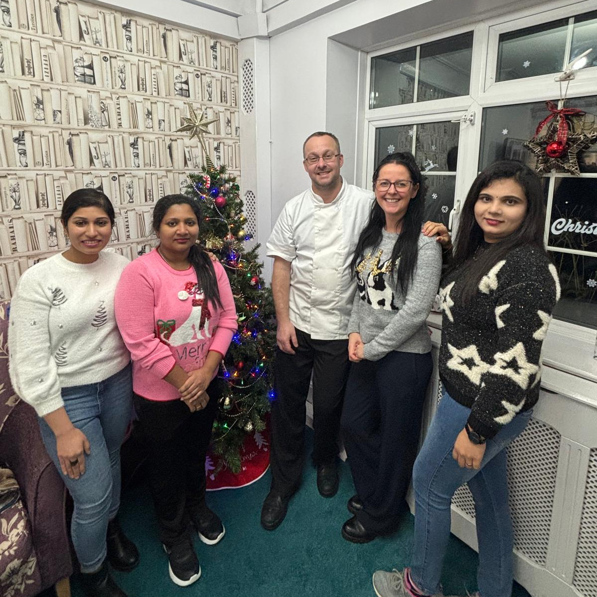 A group of people in Christmas jumpers stood in front of a Christmas tree