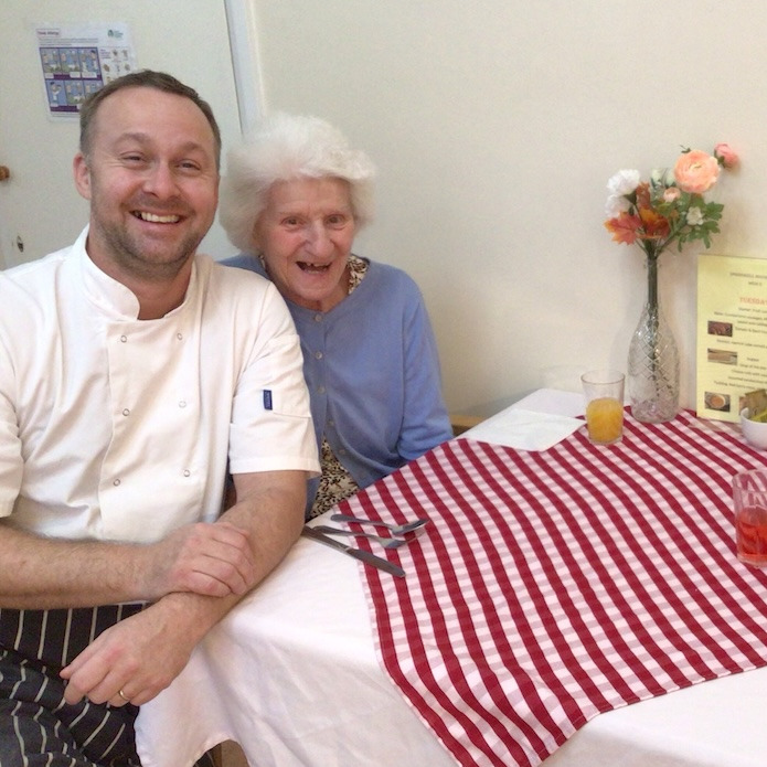 A staff member and elderly woman sat at a dining table