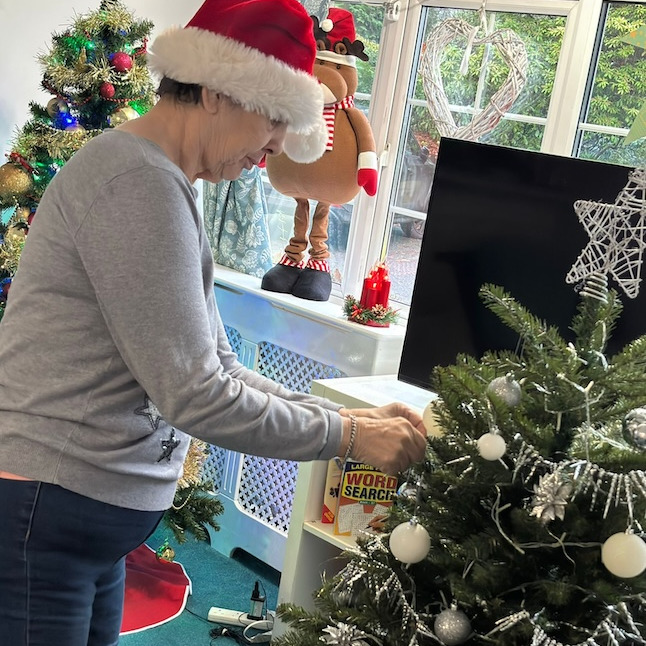 An older woman wearing a santa hat decorating a Christmas tree
