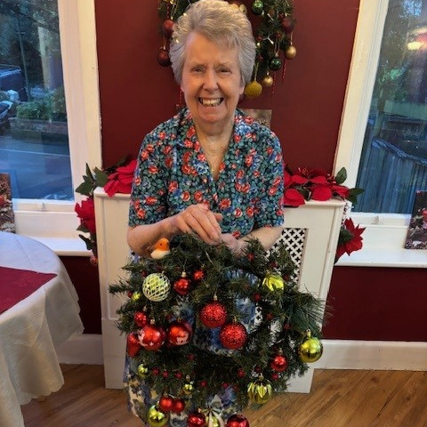 An older woman smiling holding a Christmas wreath