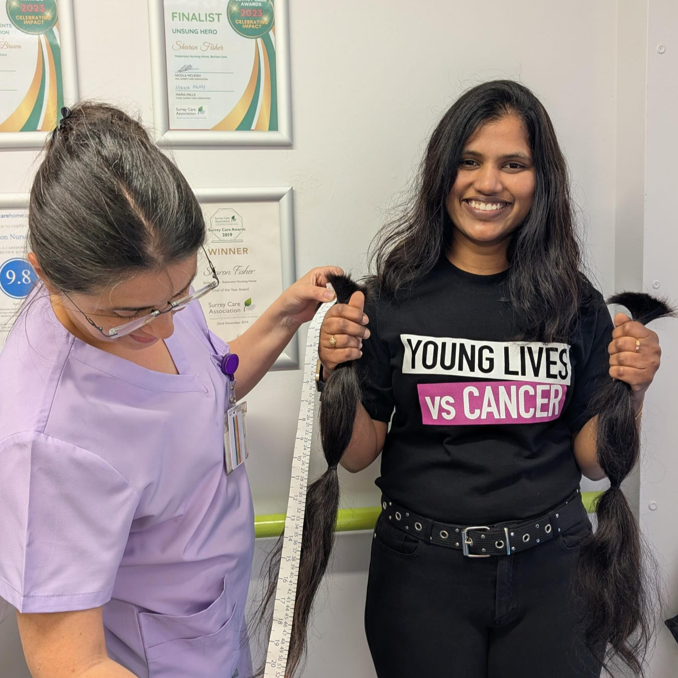 A woman holding lengths of hair while another woman measure them after a haircut 