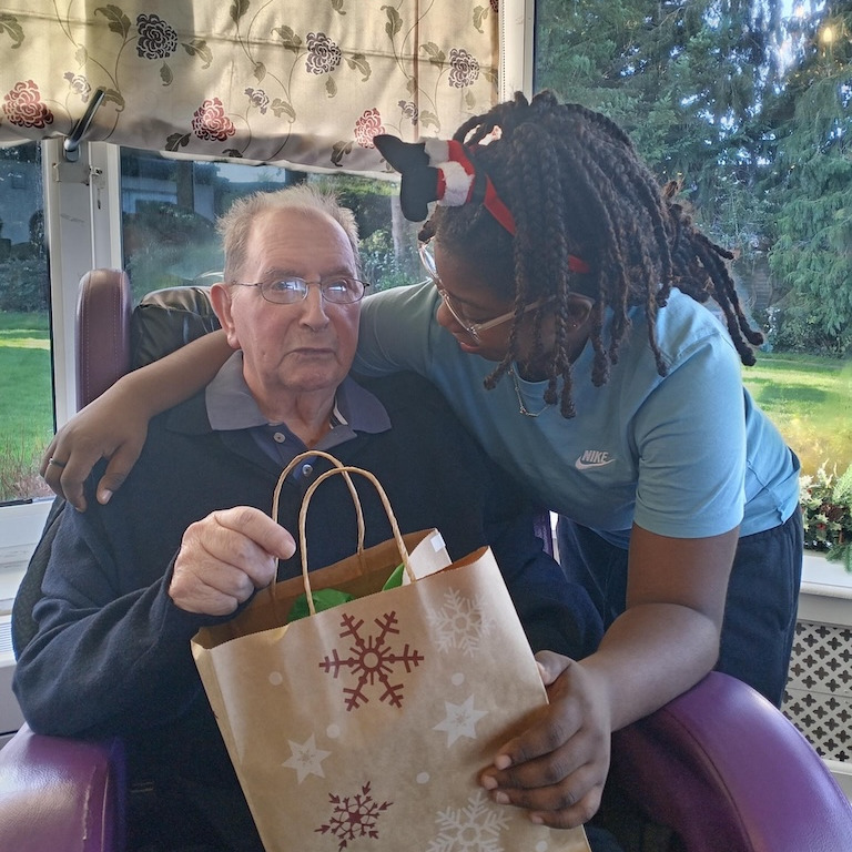 A staff member hugging a resident as he holds a Christmas present